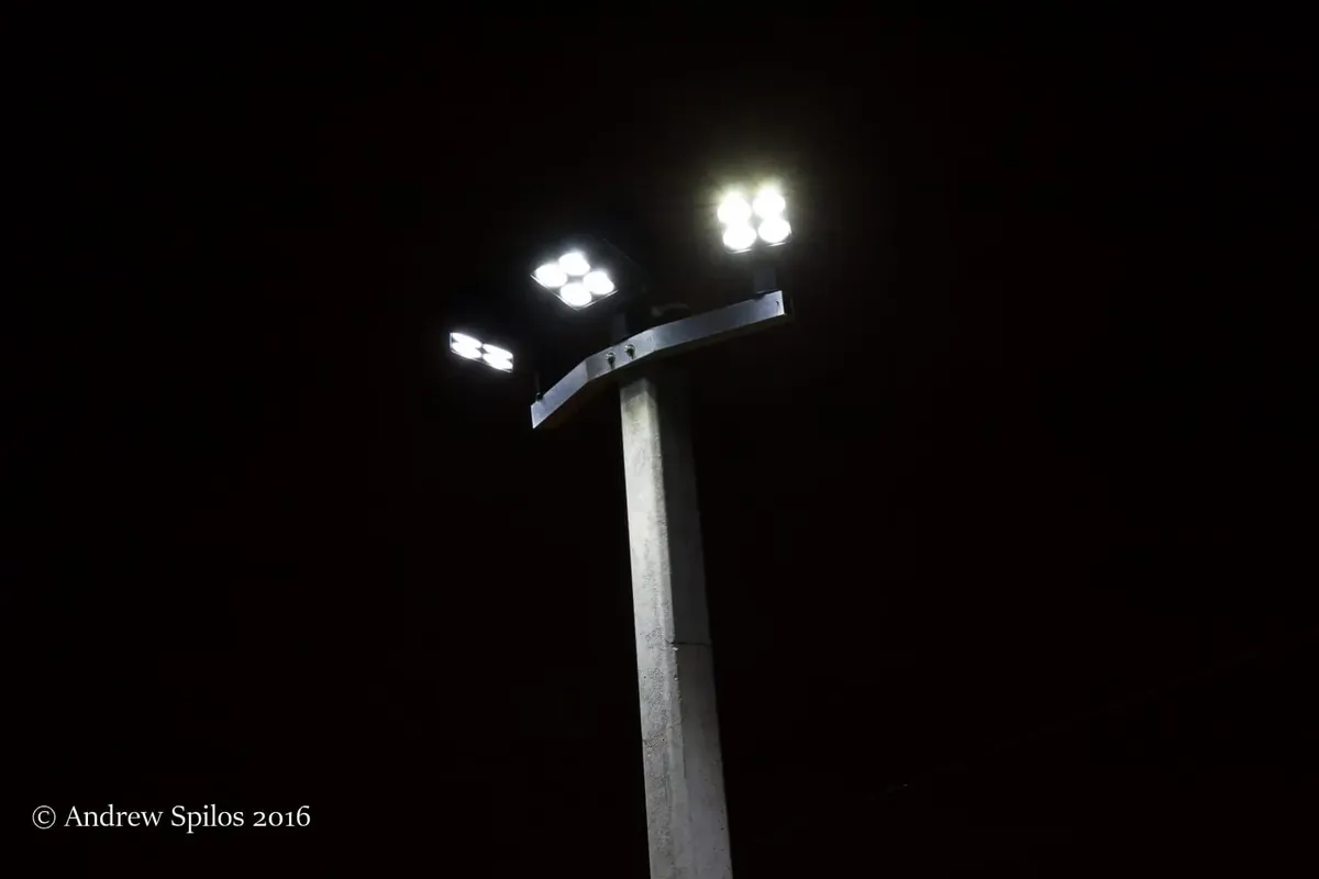 Close-Up Of A Concrete Light Pole With Four Bright Led Floodlights Illuminating The Dark Night Sky.