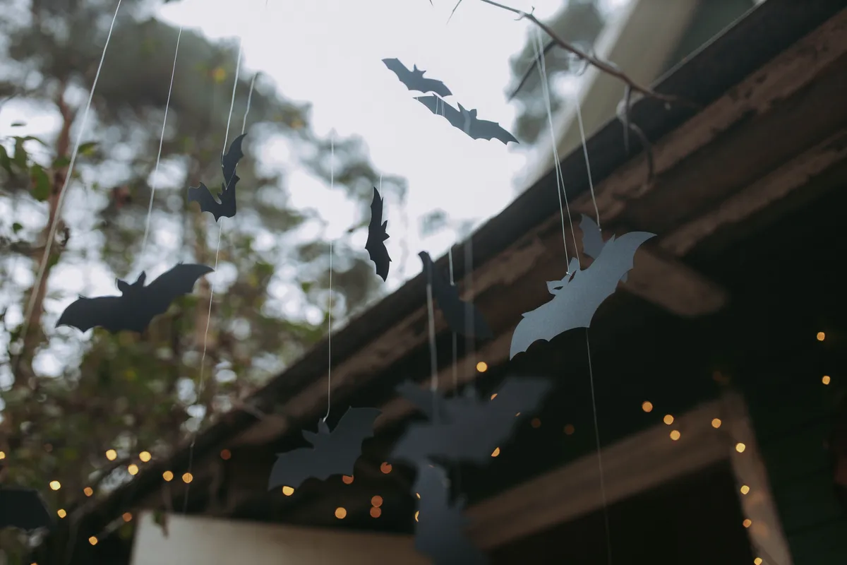 Black Bat Silhouettes Hanging From The Roof With String Lights For Halloween In The Background